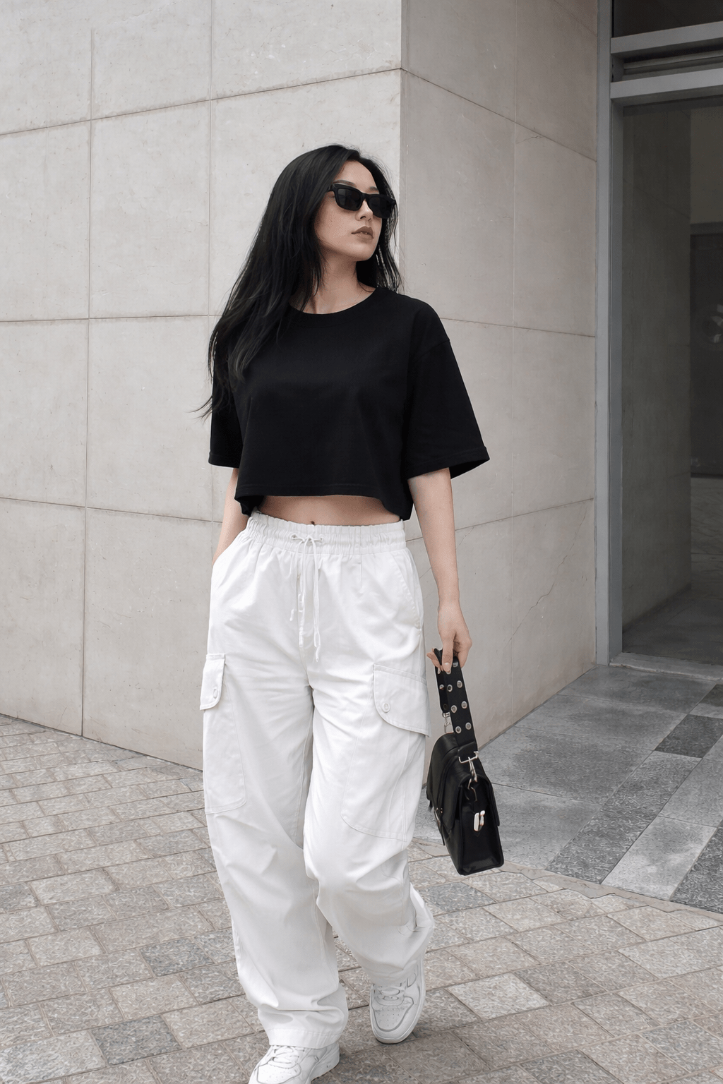 Woman wearing a black crop top and white cargo pants standing against a light-colored wall.