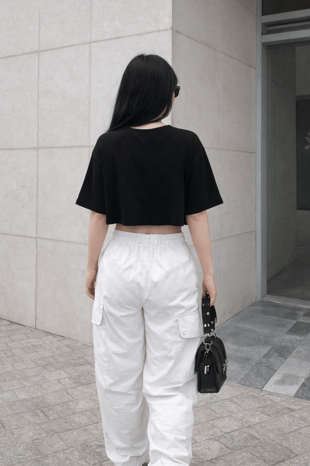 Person wearing a black crop top and white pants walking away from a building.