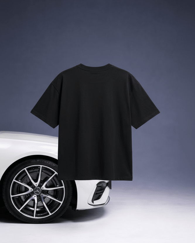 Black t-shirt held up in front of a white car on a gray background