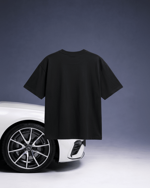 Black t-shirt held up in front of a white car on a gray background