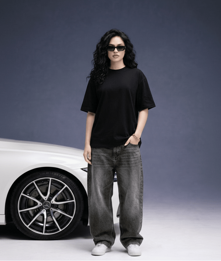 Person wearing a black t-shirt and gray jeans standing next to a car on a gray background