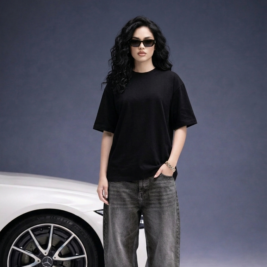 Person wearing a black t-shirt and gray jeans standing next to a car on a gray background